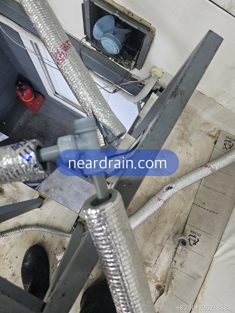 Insulated flexible hoses and a shut-off valve under a balcony boiler, mounted on a metal frame beside an exterior wall