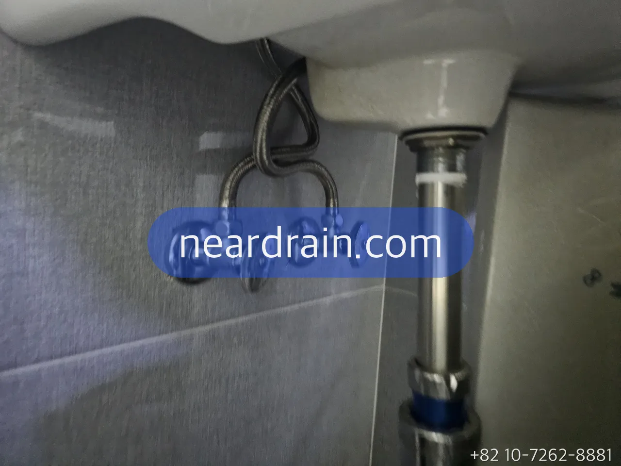 Two chrome angle valves on a tiled wall under a basin, braided hoses rising to the tap
