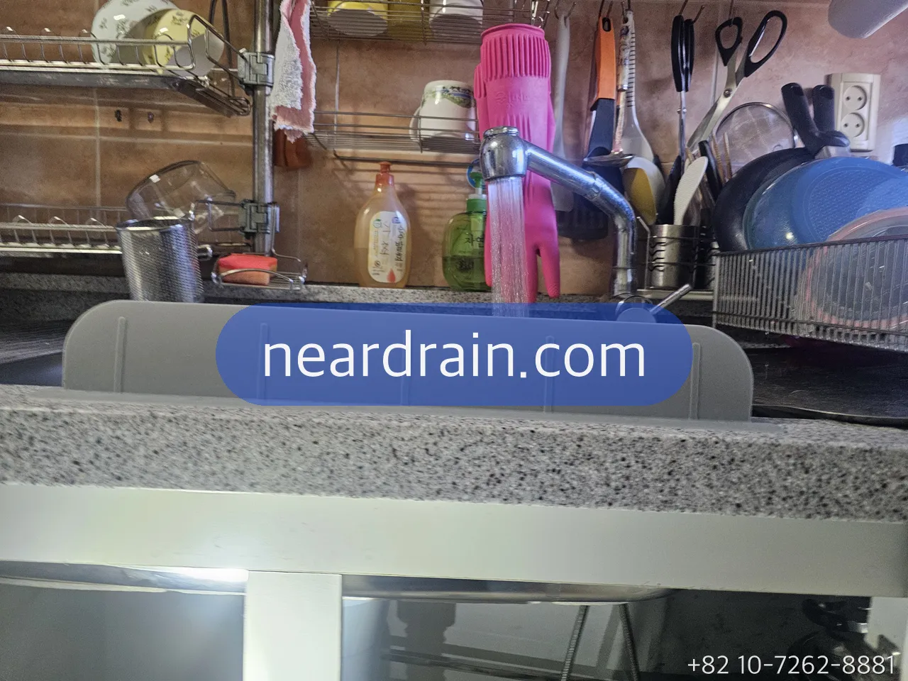 Kitchen mixer tap running a thin stream of water into a stainless sink, dish rack and utensils behind