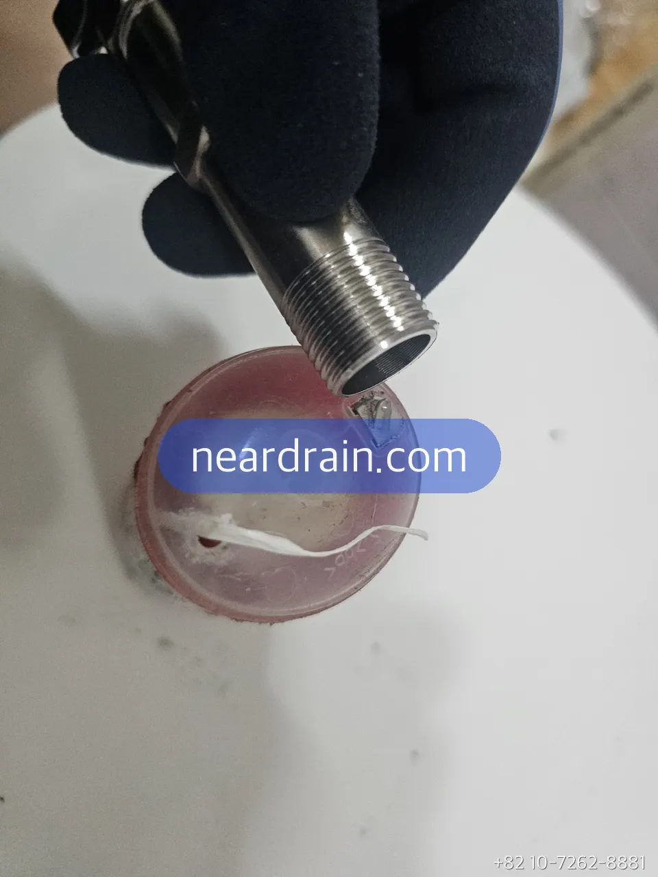 Gloved hand holding a threaded shower hose fitting above a clear pink shower filter housing with a used cartridge inside