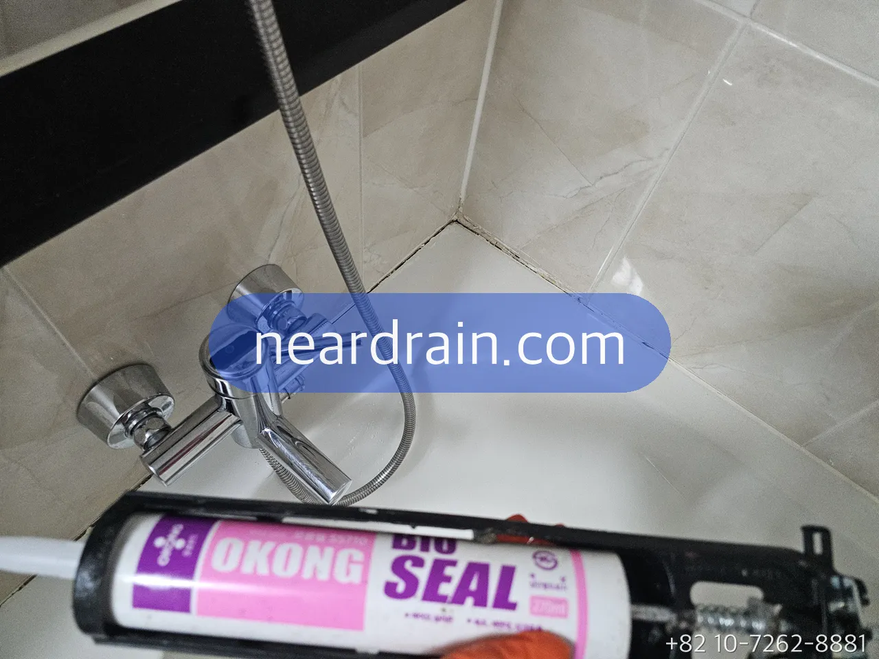 New chrome shower mixer fitted on beige tile above a bathtub, silicone sealant gun in the foreground