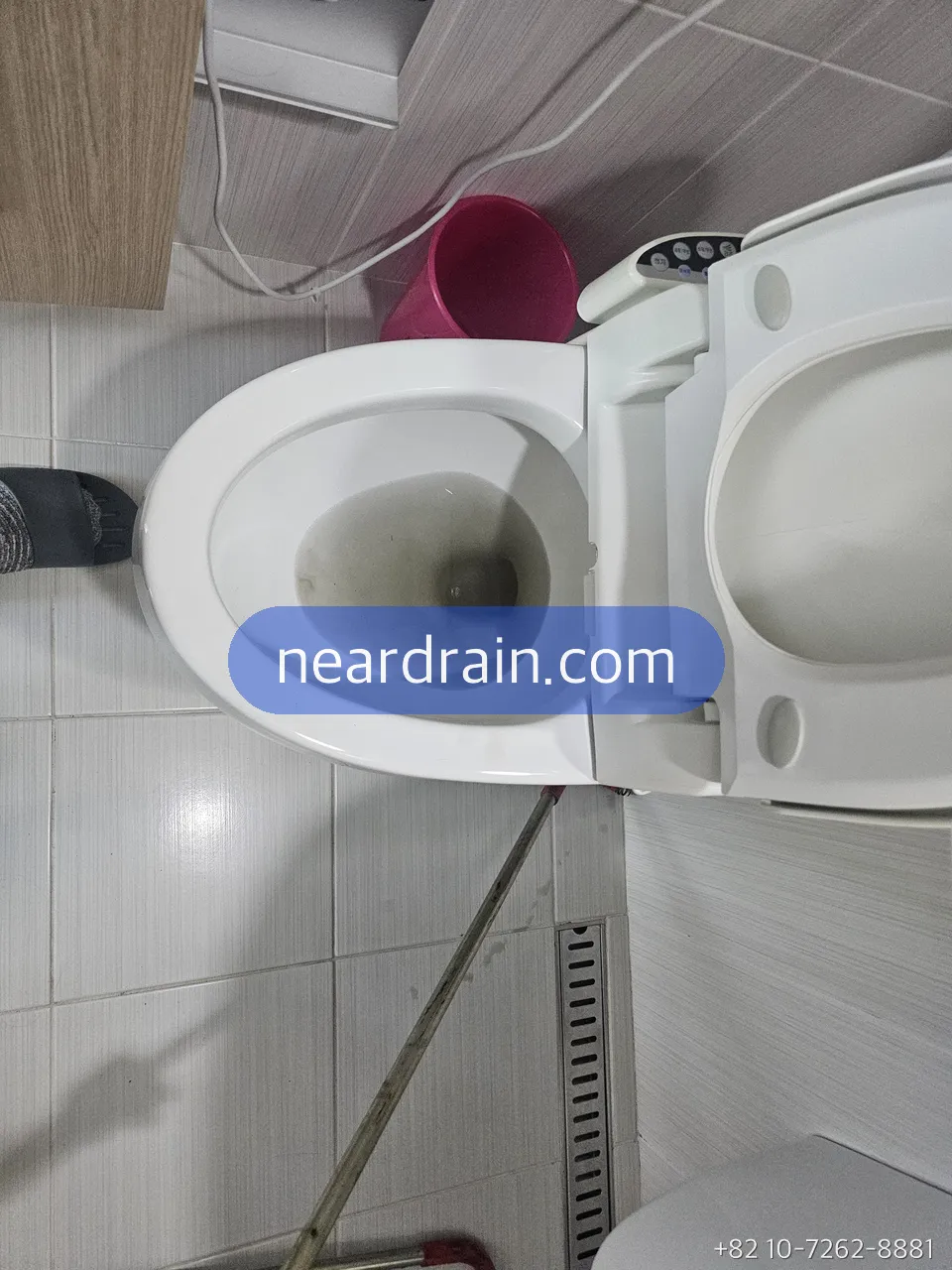 水位が上がったまま引かない便器、タイル床の浴室、ピンクのバケツが横に置かれている