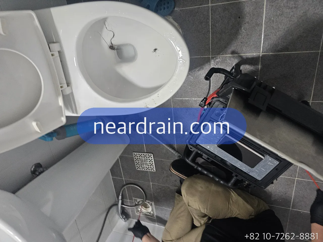 便器の横に配管カメラのモニターを置き、上から便器と排水口を映している作業中の様子
