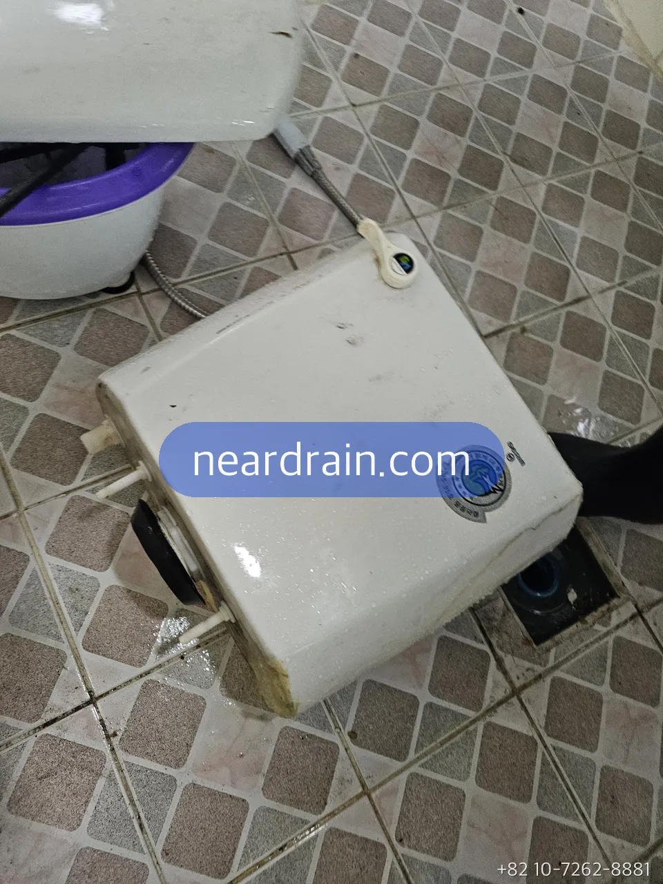 Korean two-piece toilet tank lifted off and set on the bathroom floor, fill valve and supply fittings visible underneath