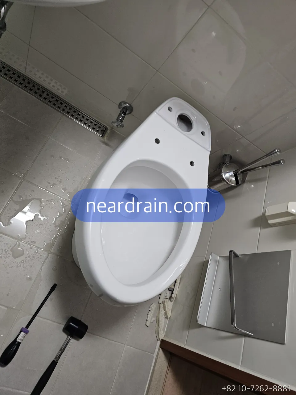 Toilet bowl with its tank removed in a small tiled bathroom, tools laid on the floor